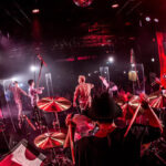 赤い照明のライブステージで演奏するバンド